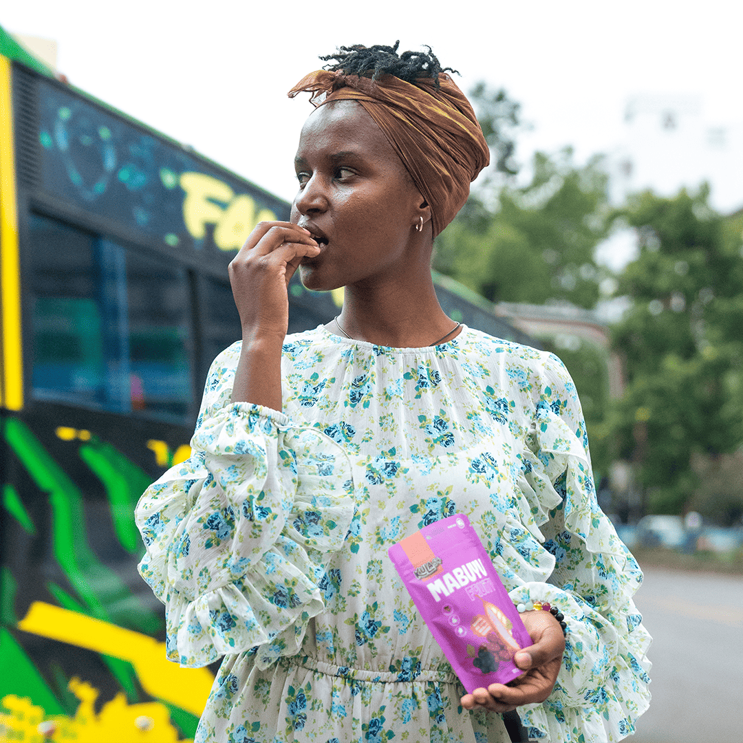 Woman holding Kula54 Mabuyu Fruity package, a Mabuyu in hand, with a blurred bus in the background

Location: Nairobi, Kenya