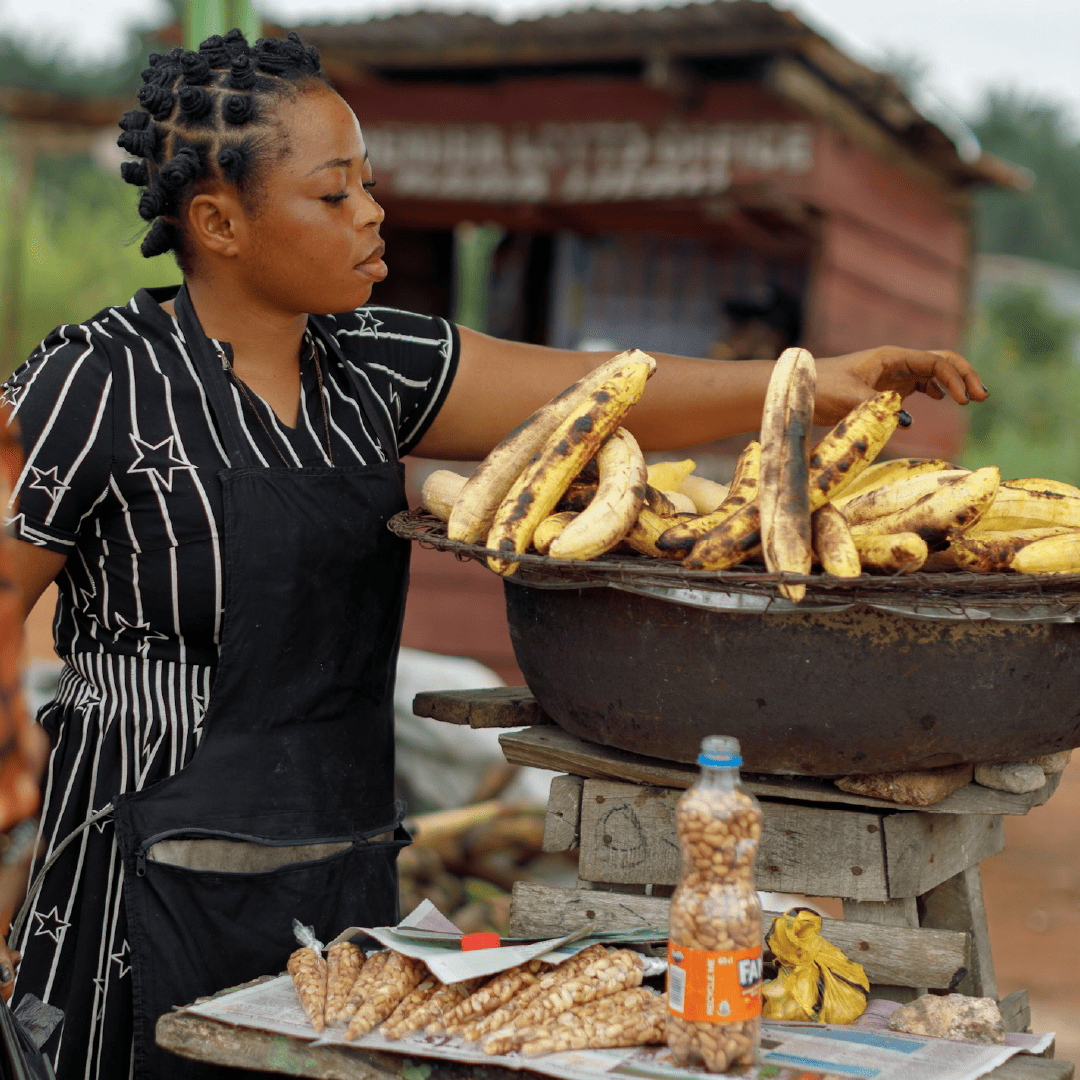 Woman selling roasted plantains at an outdoor market.

Image by: Ben Iwara