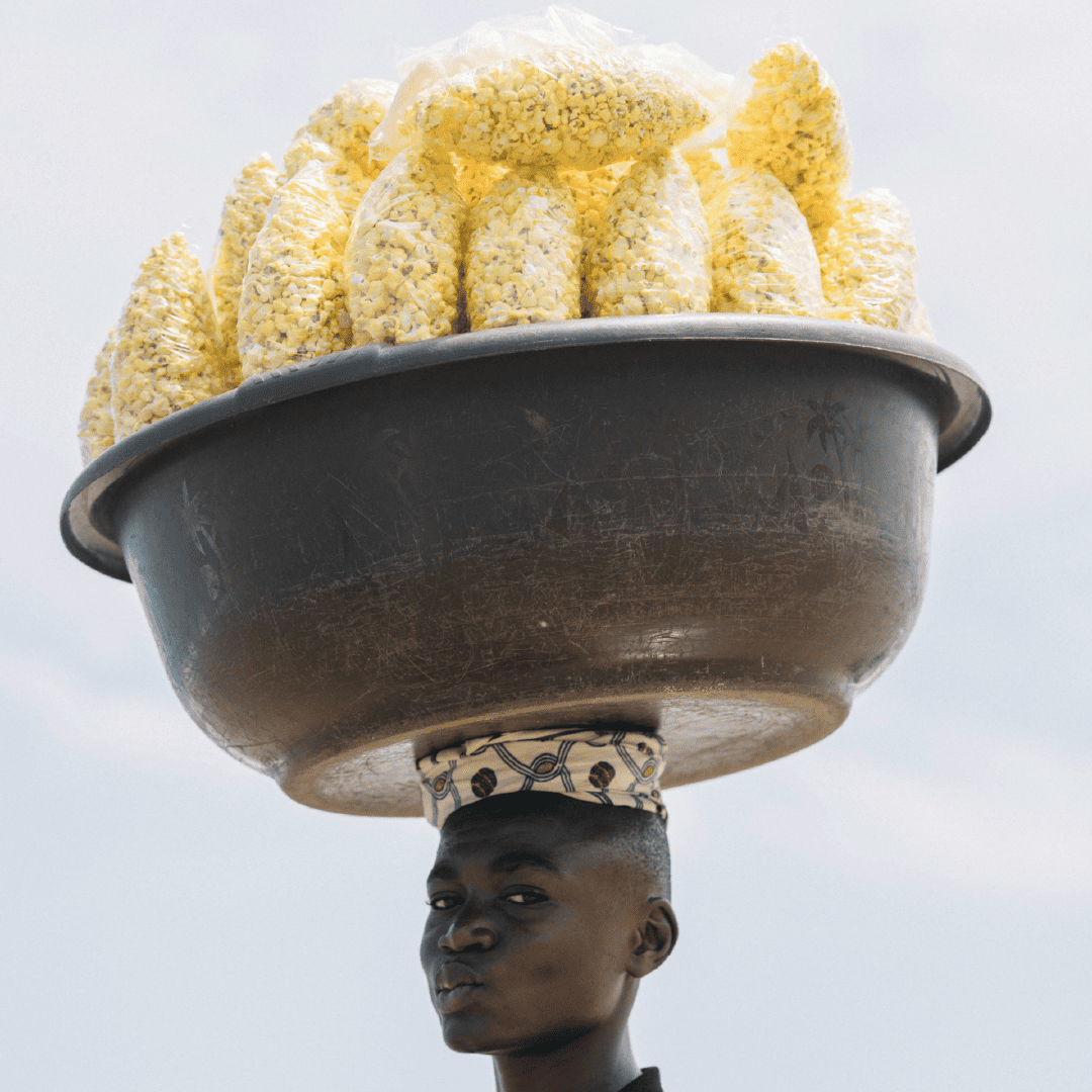 Male carrying a large bowl on their head with filled with individually packed bags of popcorn.

Image by: Random Institute